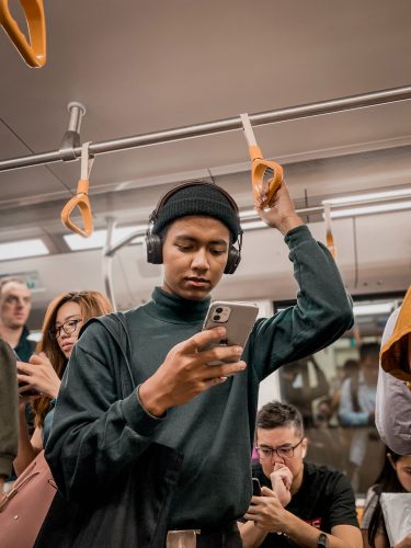 A person on a train looking at their phone. Other people are on their phones behind that person.