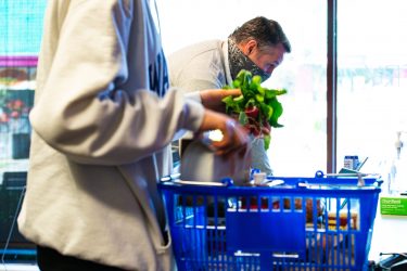 person placing radishes in a blue shopping basket