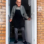 Elderly man opening front door to find a bag of food on his doorstep