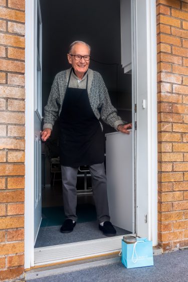 Elderly man opening front door to find a bag of food on his doorstep