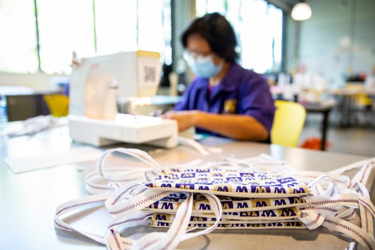 man using sewing machine with pile of cloth masks in foreground