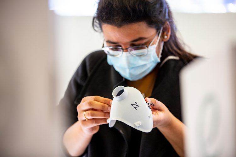 woman inspects a white piece of plastic shaped like a mask with a hole in the center