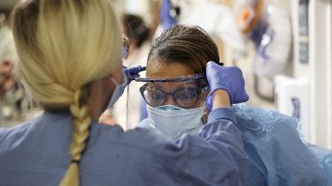 health care workers helps take protective glasses off another