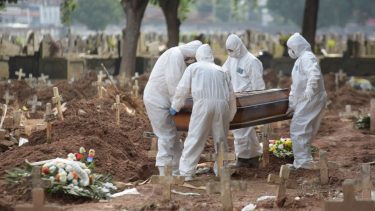 people in hazmat suits put a coffin in the ground