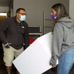 Man and young woman carry small fridge into dorm room