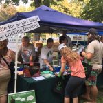 visitors approach a booth with volunteers at a park