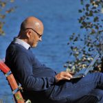 older man sitting on park bench with laptop