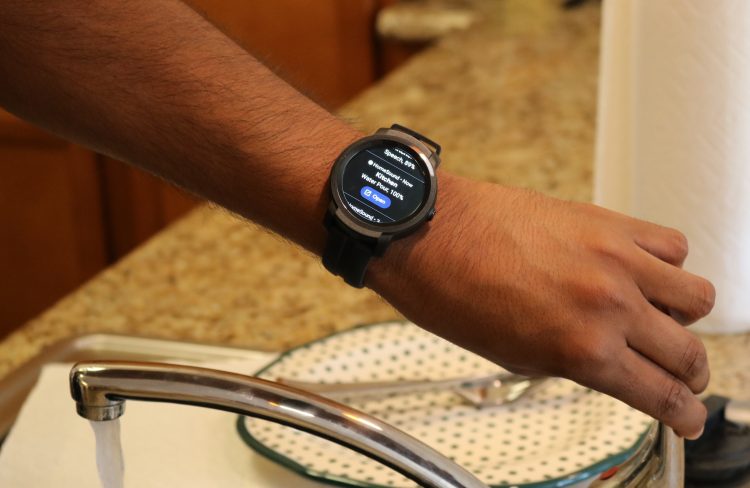 A hand turning off a faucet. There is a smartwatch on the person's wrist that is giving information about the sound of the water in the sink.