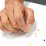 A hand picking up a tiny bead