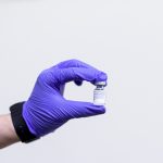 gloved hand holding up a vial of a vaccine