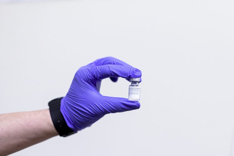 gloved hand holding up a vial of a vaccine