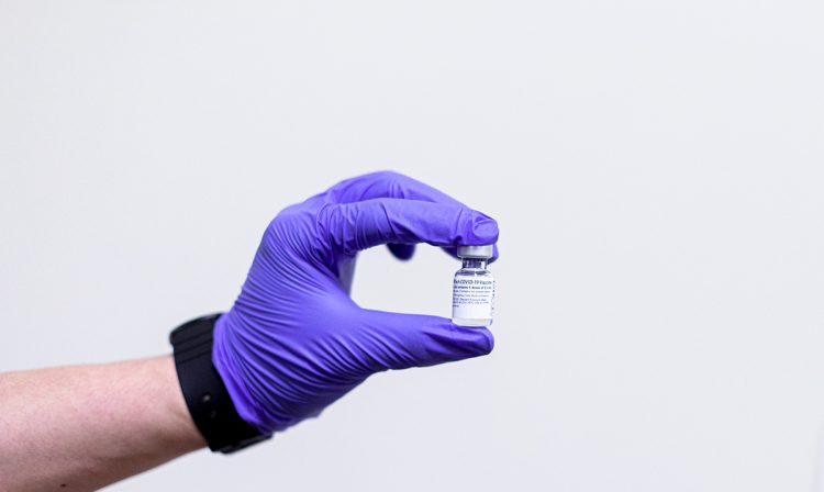 gloved hand holds vial of vaccine