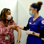 Woman in scrubs pats woman rolling up shirt sleeve