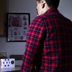 A small white box on a table and a person sitting in front of it (their back is to the camera)