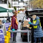 Woman gives a box of masks to a donation drive at a UW parking lot.