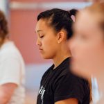 Students standing silently, eyes closed, in a yoga or meditation class