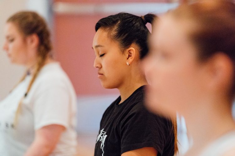 Students standing silently, eyes closed, in a yoga or meditation class
