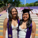 Two students pose for graduation pictures in front of staircase decorated for commencement.