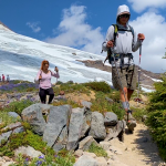 Two students are on a rocky with hiking poles and a glacier in the background.