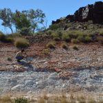 person crouching in distance on layered rock