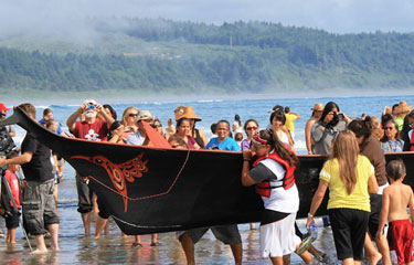 People watching a long boat being carried out of the water