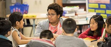 Students and teacher sit in at a table in a classroom