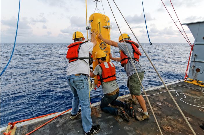 Engineers attach a pod that will zoom up and down along the yellow cable in water at the base of the Axial undersea volcano.