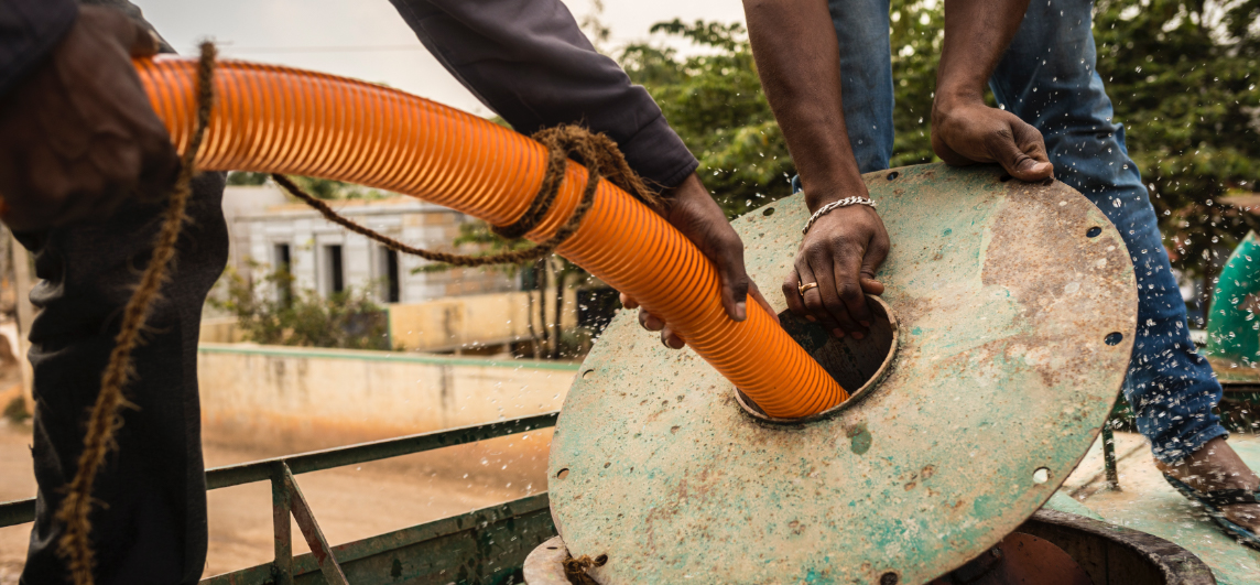 Using a hose, men fill a tanker truck with water pumped out of a deep aquifer — a layer of underground permeable rock, gravel or sand that holds water.
