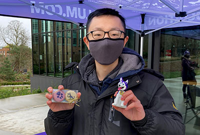 Member poses in front of UWAA pop-up, holding 2 give-away items.
