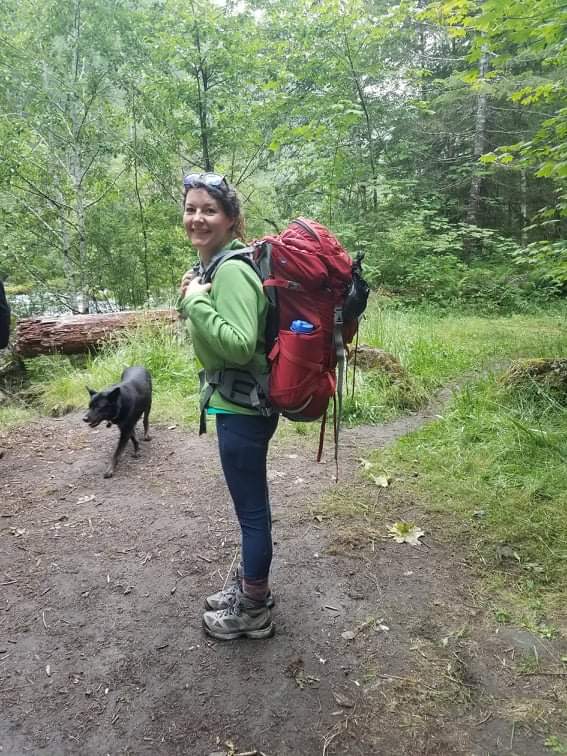 woman in green coat with red backpack getting ready to hike.