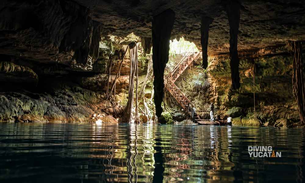 Interior del cenote Calcuch con paredes de roca y entrada limitada de luz natural.