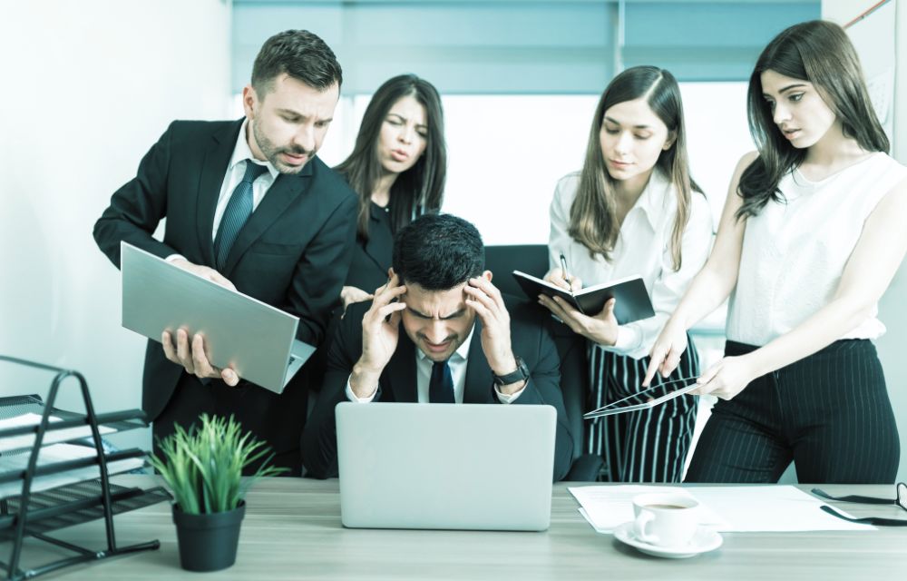 Dueño de pyme estresado junto a equipo de trabajo en oficina, comparando liderazgo con caos
