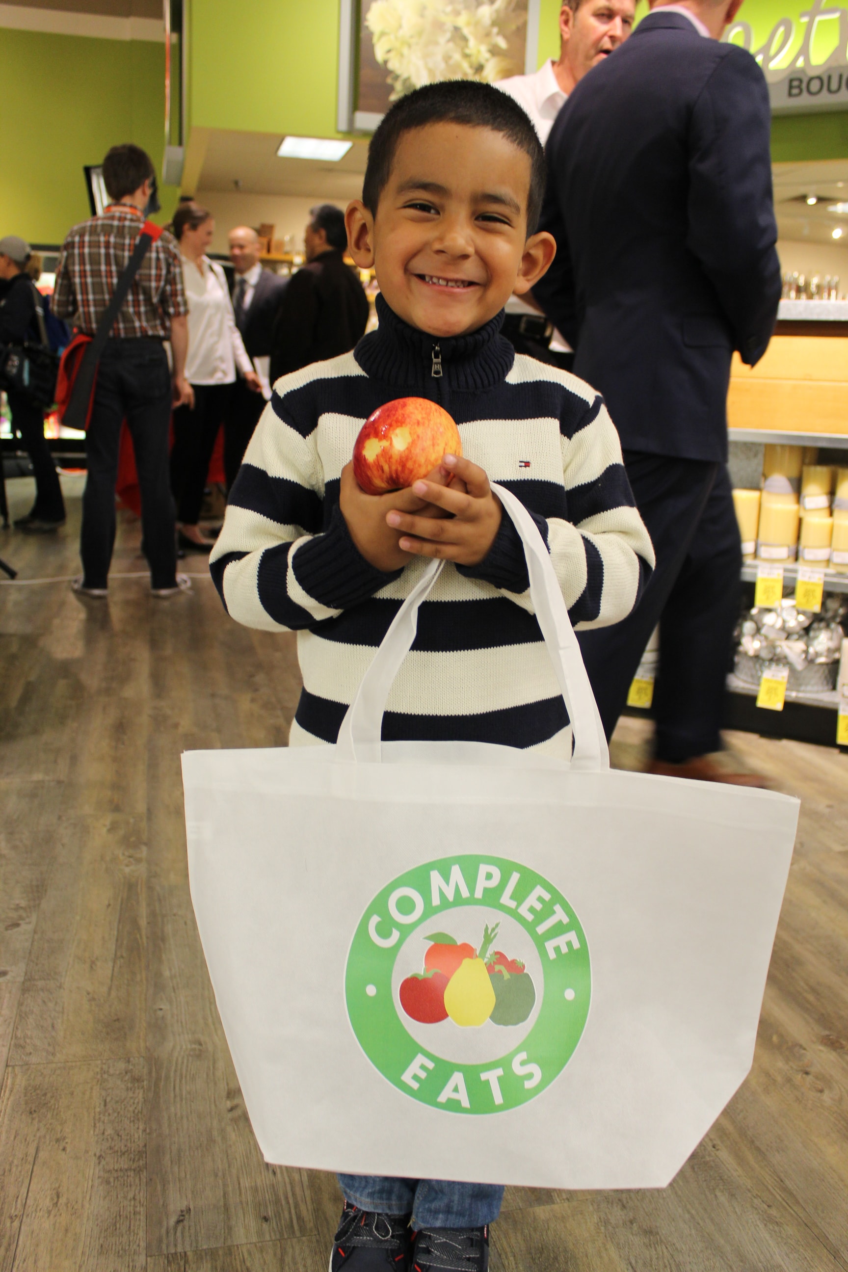 Little boy holding apple and Comple Eats shopping bag.