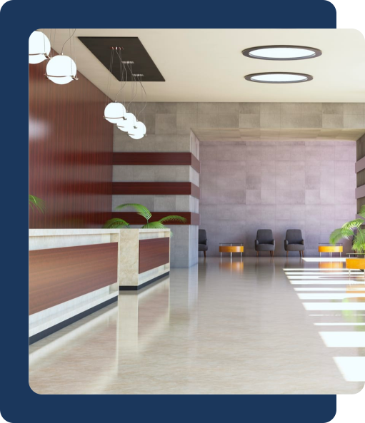 A bright office lobby with front desks, plants and some chairs on the back wall.