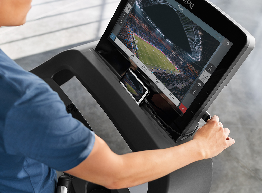 A person in a blue workout shirt using hdmi cord to connect to console from the right side of the screen.