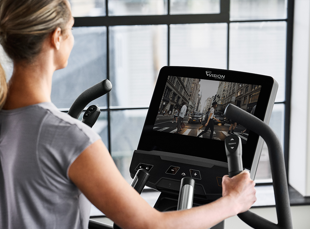 A person in a grey workout shirt working out on a Vision elliptical watching live tv on the entertainment console.
